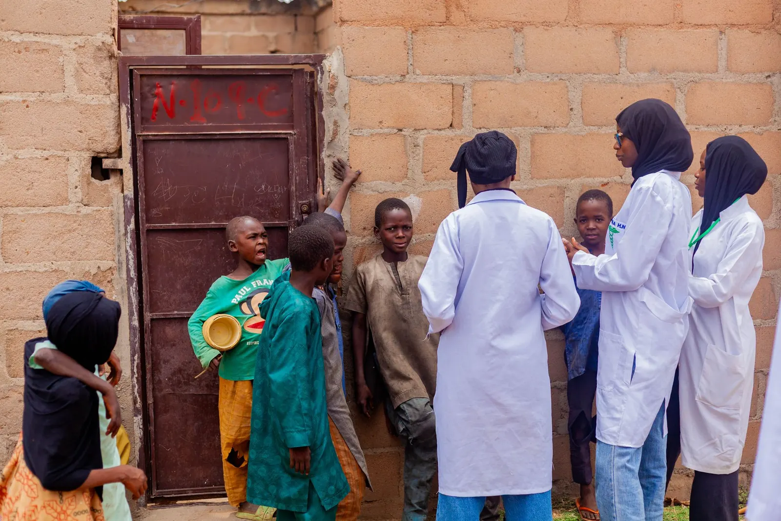 Health workers in hijabs and white coats talking with children outside a home