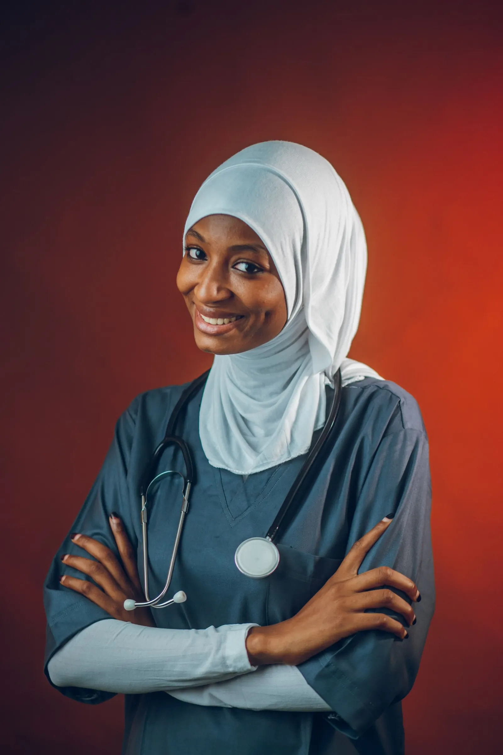Smiling female doctor in a hijab and scrubs with a stethoscope, arms folded